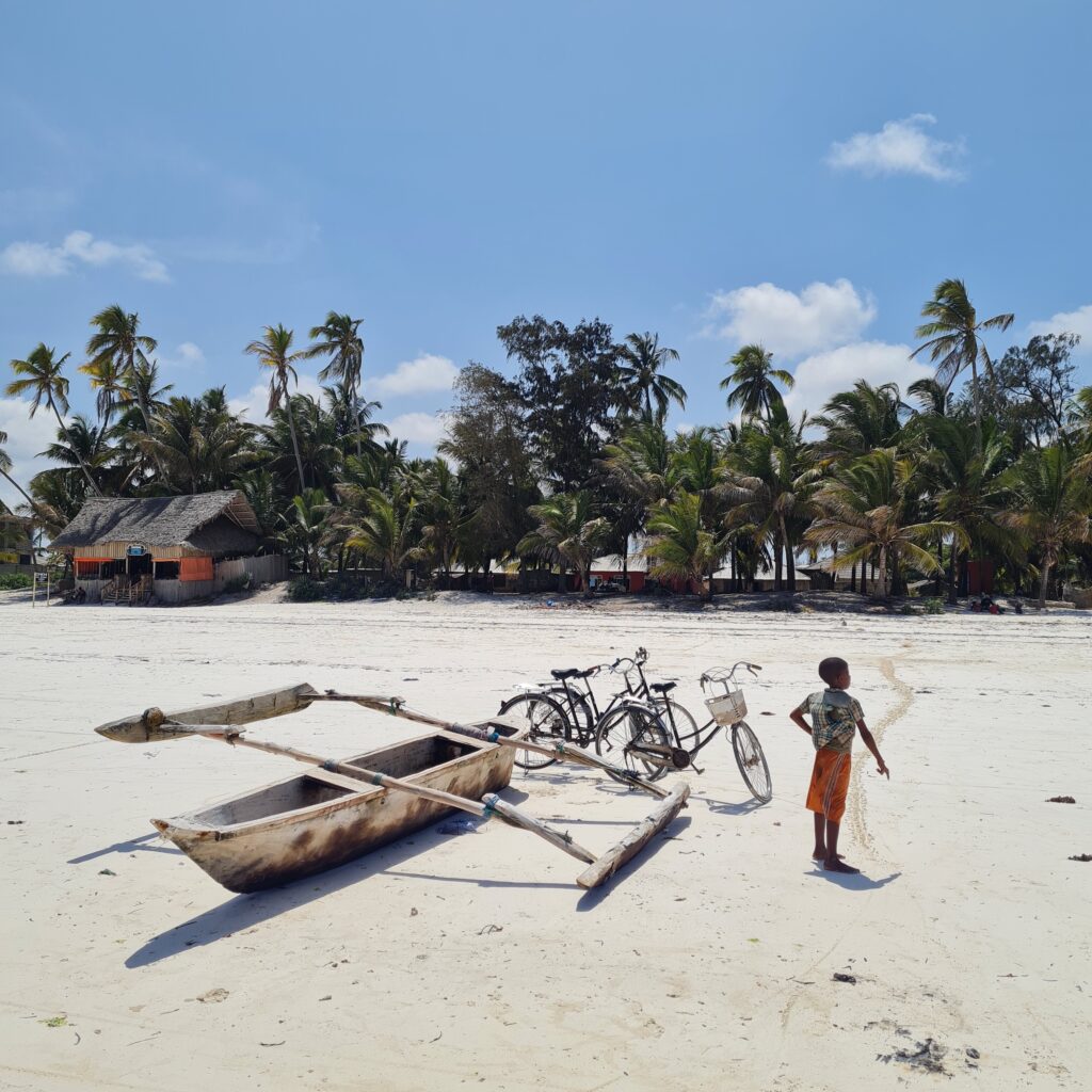 Enfant, bateau de pêcheur et vélo sur une plage de sable blanc à Zanzibar en Tanzanie.